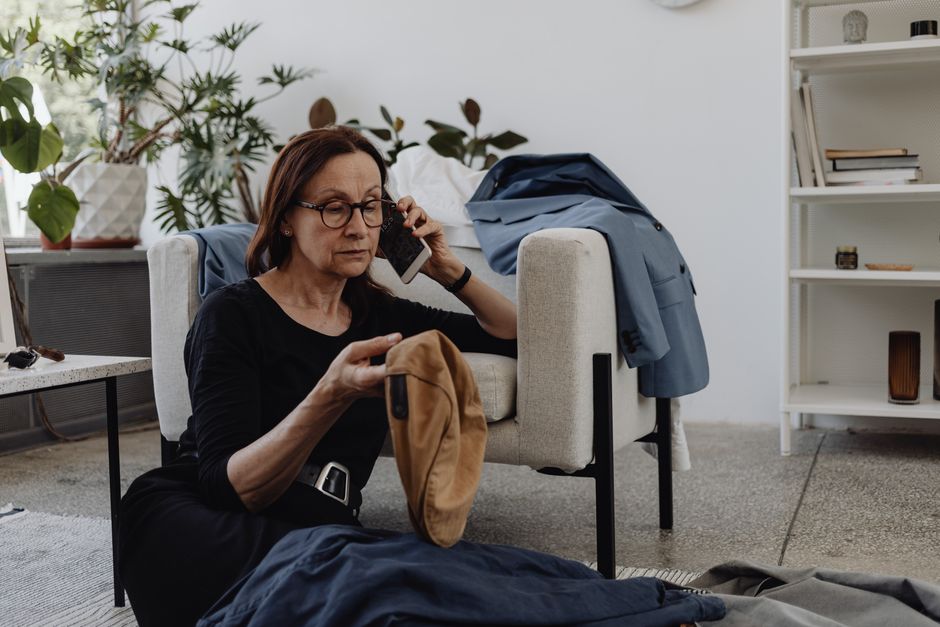 Senior woman talking on phone while organizing clothes indoors.