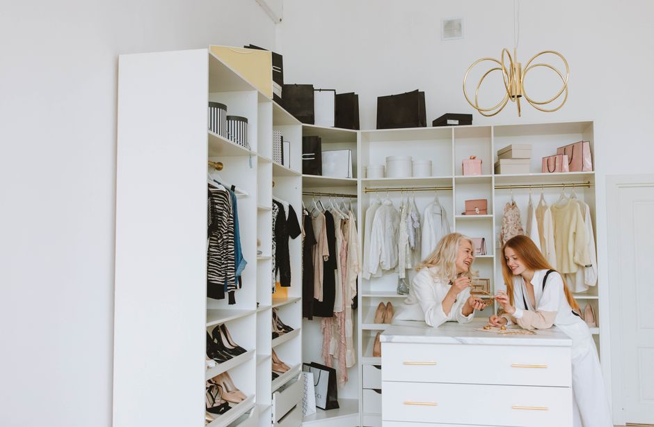 Two women talking and smiling in a chic walk-in closet with clothes and accessories.