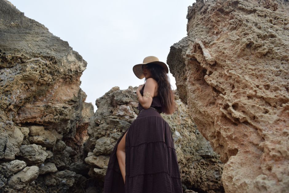 Elegant woman in a flowing dress poses amidst rugged rocks, capturing a sense of adventure.