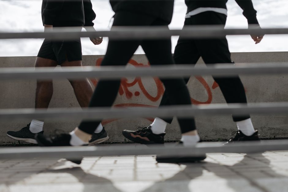 Low angle view of three people walking past a graffiti-covered wall, captured through bars.