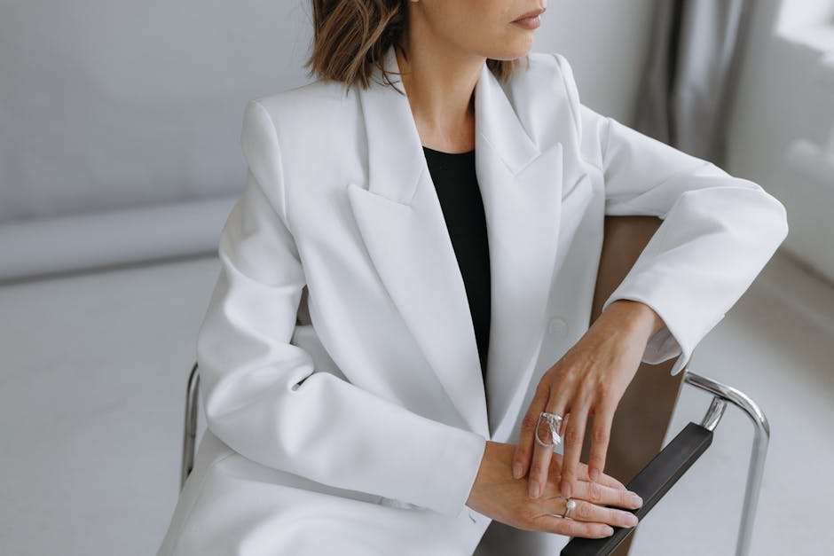 Stylish woman in a white jacket posing elegantly indoors with minimalistic decor.