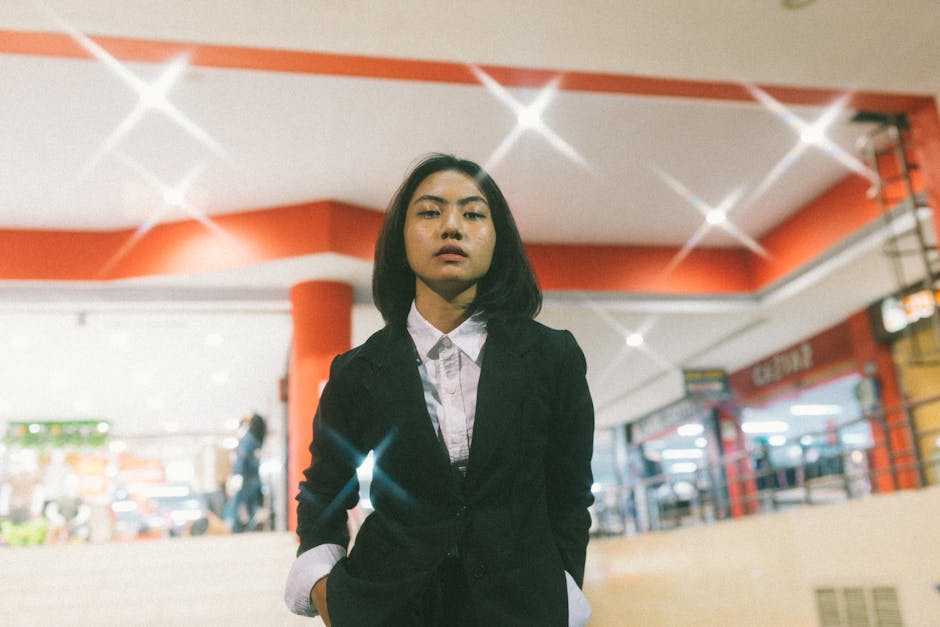 Asian woman in a black blazer posing confidently in a brightly lit indoor setting.