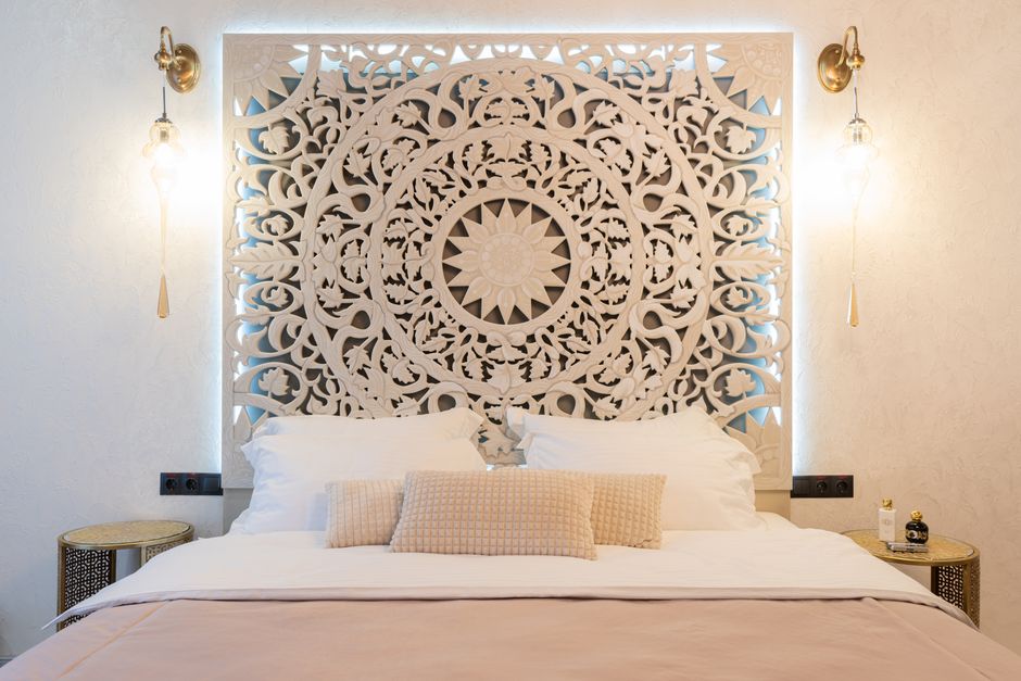 Soft bed with assorted pillows against wall with geometric ornament between glowing lights at home