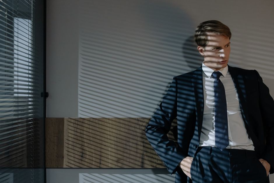 Businessman in suit, relaxed in office with dynamic shadow patterns from window blinds.