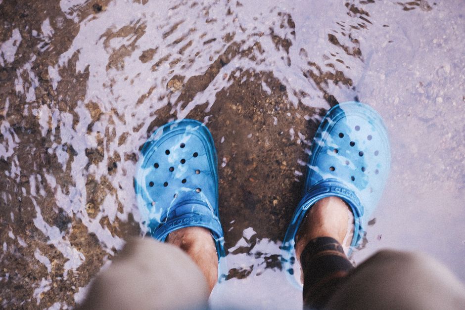 Close-up of blue shoes in a shallow stream, showcasing casual waterproof footwear.