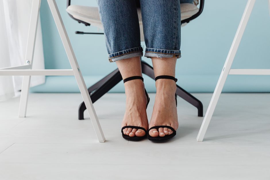 Stylish close-up of a woman wearing black high heels, jeans, and sitting on a chair.