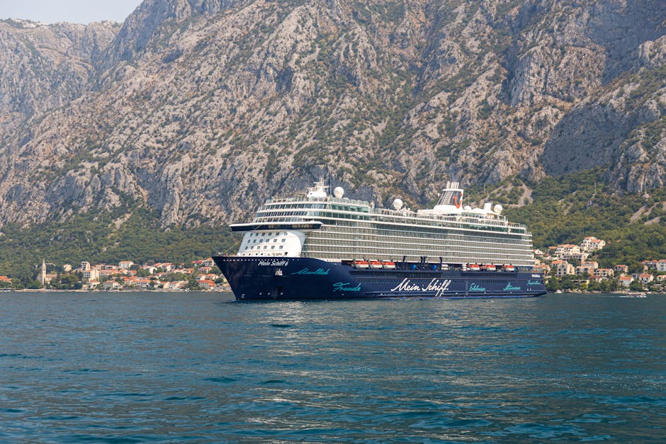 A luxury cruise ship sails against stunning coastal mountains and a serene seaside village.