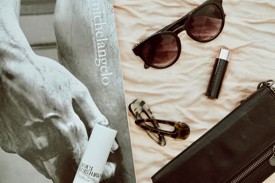 Stylish fashion accessories on display with a Michelangelo artwork in the background, creating a chic flat lay.