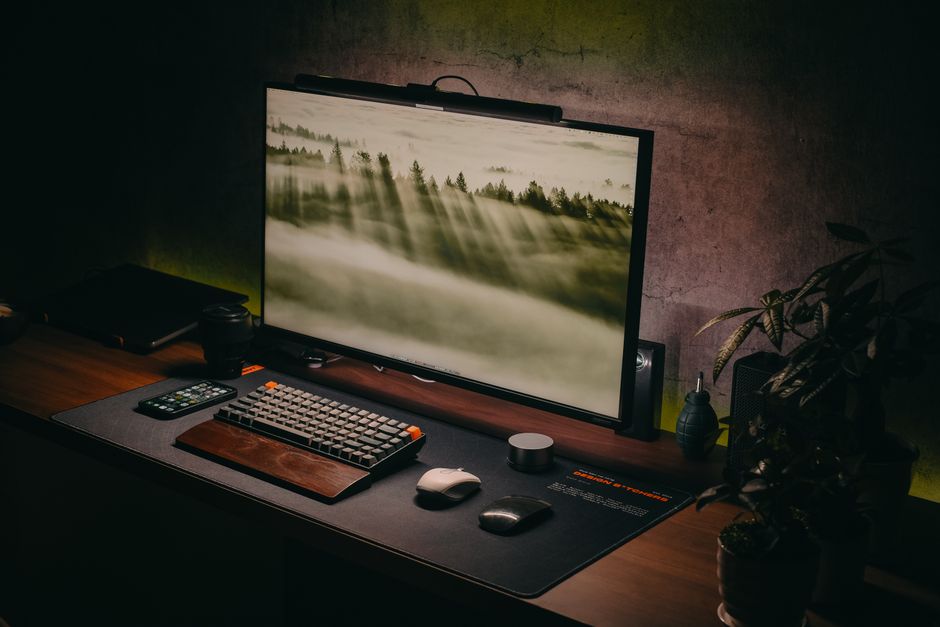 A modern and stylish computer setup with a keyboard, monitor and accessories on a wooden desk in a cozy home office.