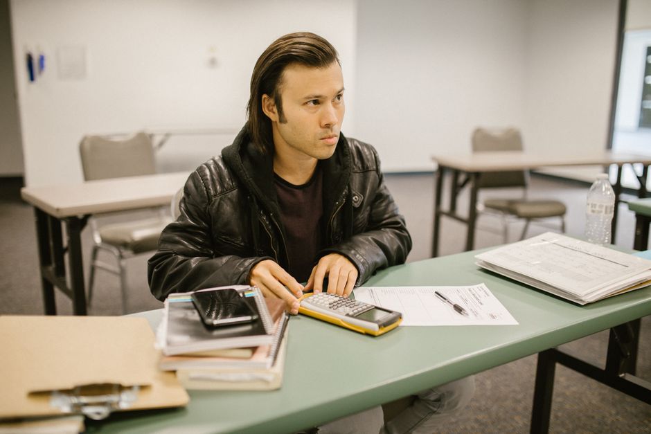 A focused young man using a calculator while studying in a classroom setting.