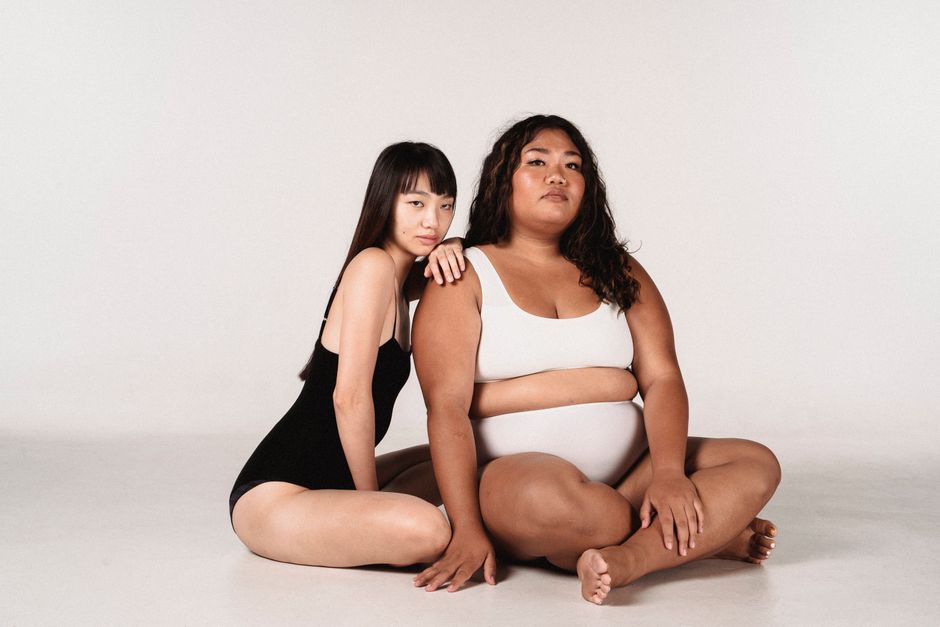Full body of young Asian models with different sizes in underwear relaxing on floor in studio and looking at camera