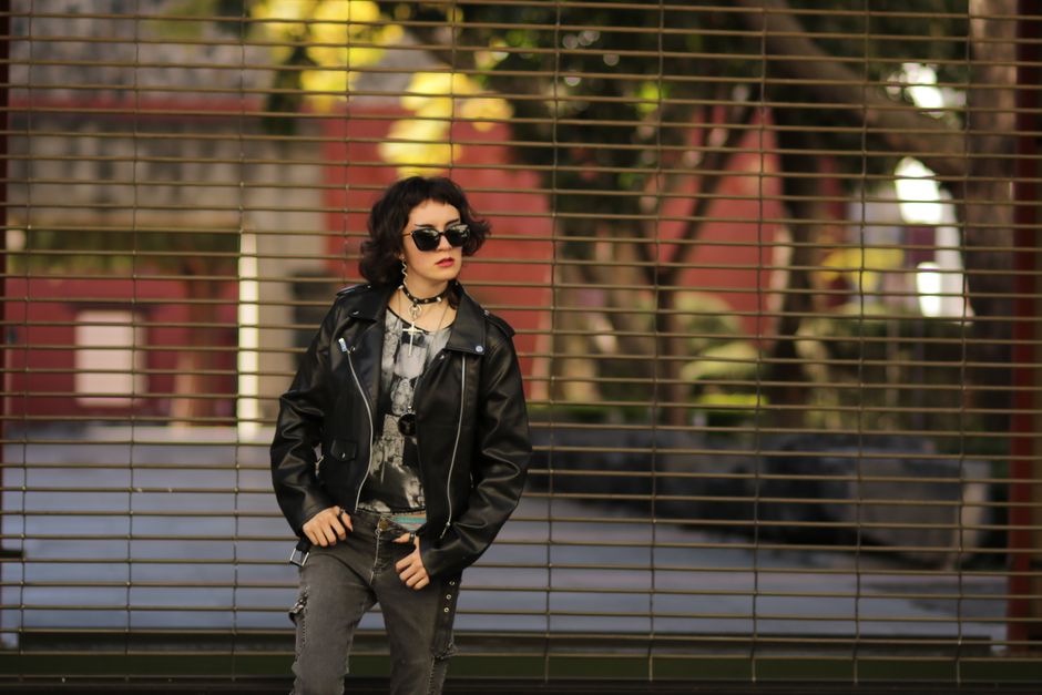 A stylish woman wearing a leather jacket poses confidently outdoors.
