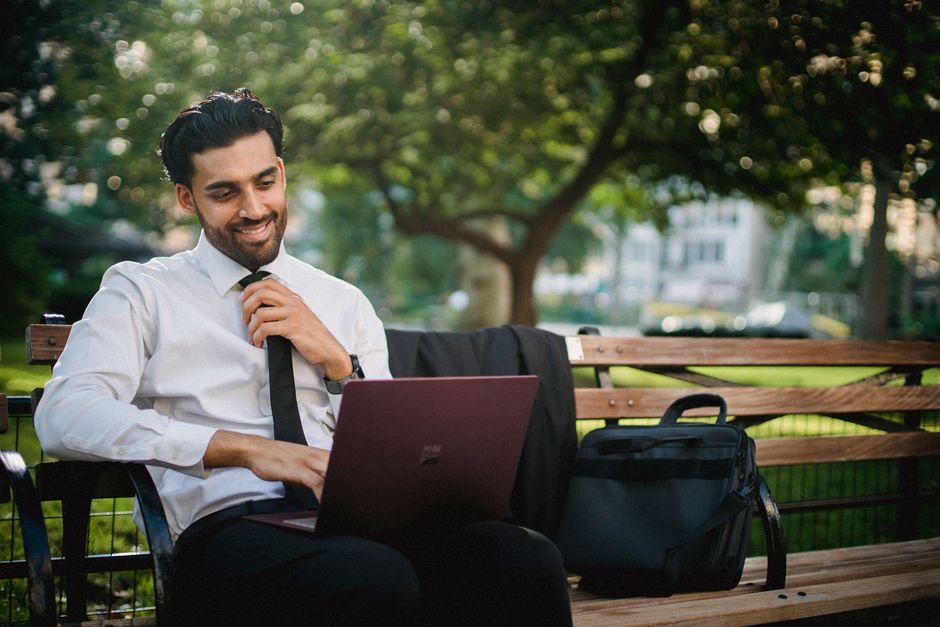 A smiling businessman working on a laptop in a tranquil park setting, embodying remote work freedom.