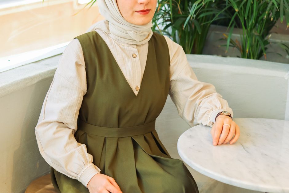 Woman in a green dress sitting at a café table with indoor plants.