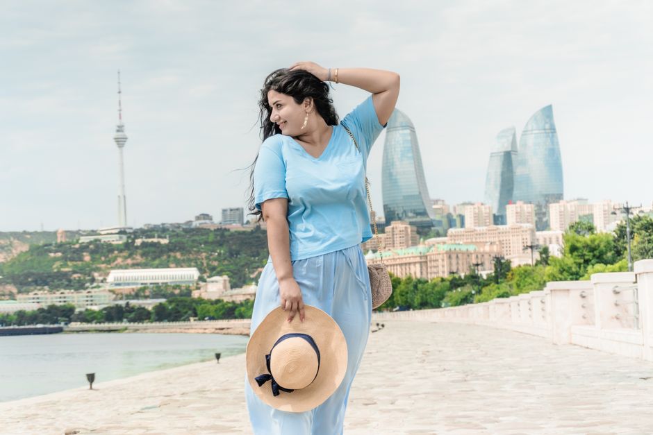 Elegant woman posing with a hat near Baku's Flame Towers.