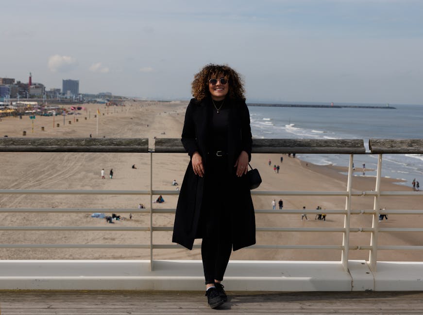Woman in black standing on boardwalk overlooking the beach on a clear day.