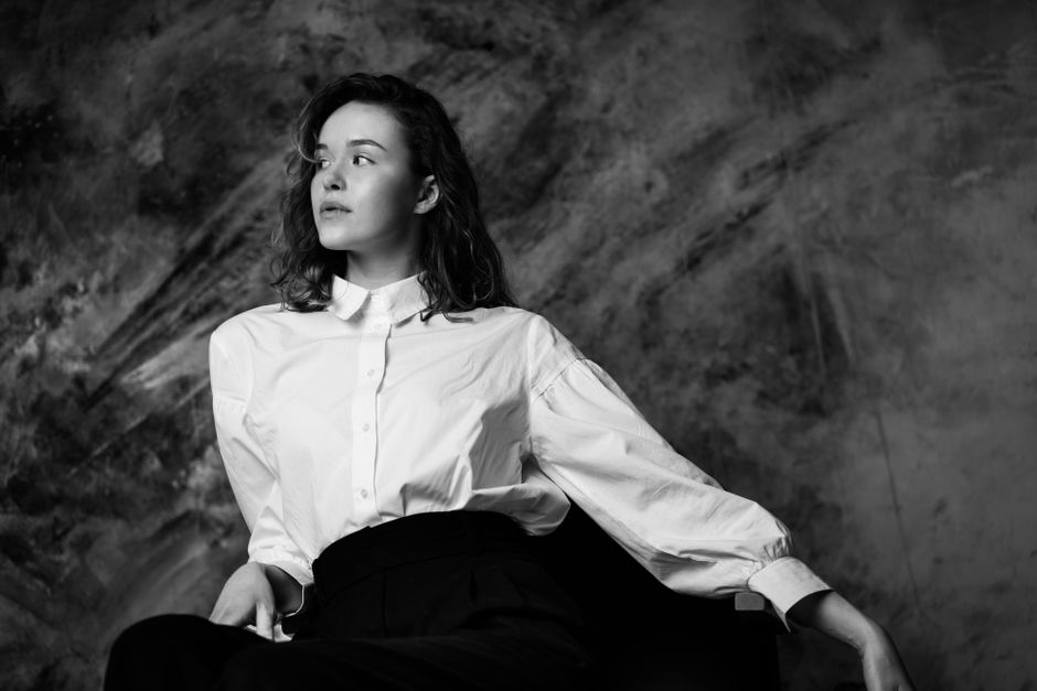 A striking black and white portrait of a woman in a white shirt, gazing thoughtfully.