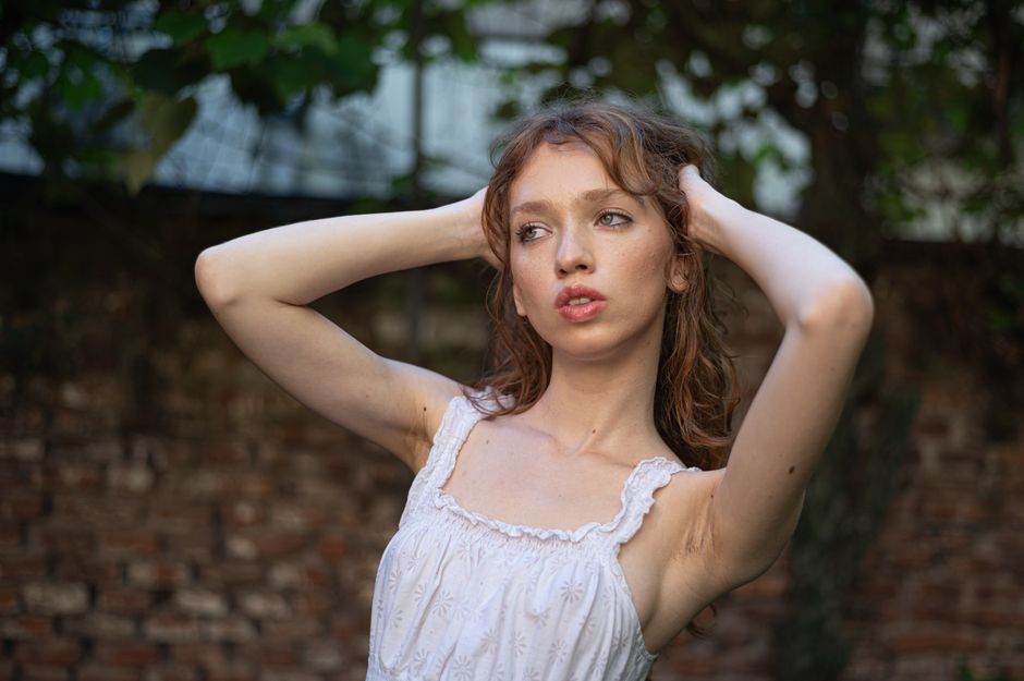 Portrait of a young woman with auburn hair, posing outdoors in a summer setting.