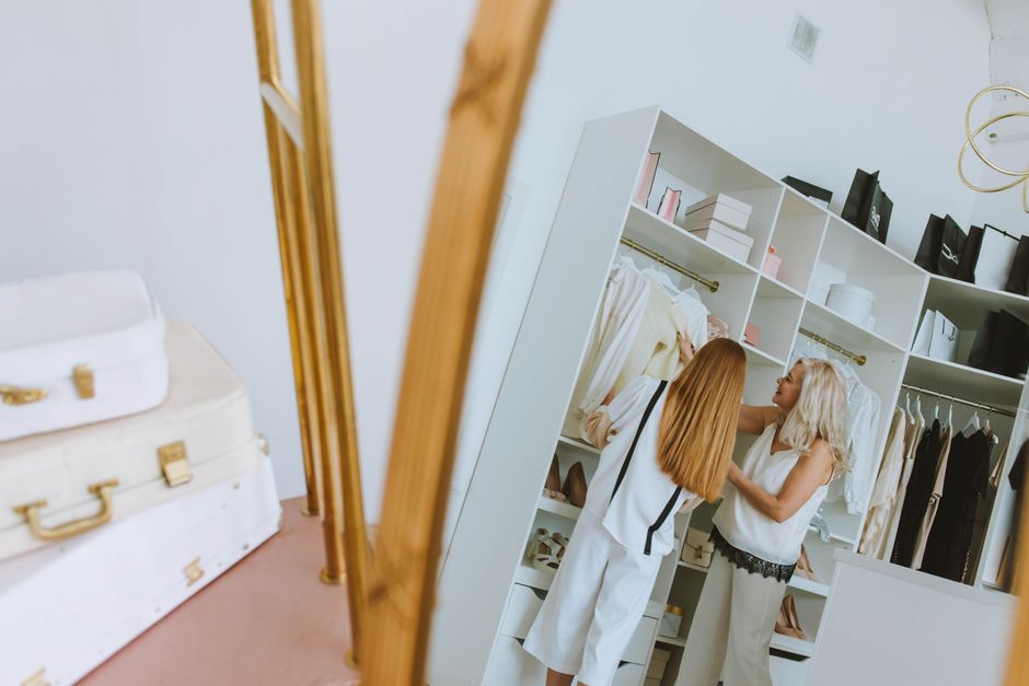 Two women selecting clothes from a stylish wardrobe in a chic room setting.