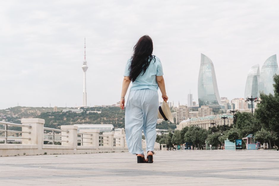 A woman walks along Baku boulevard with the iconic Flame Towers in the background.