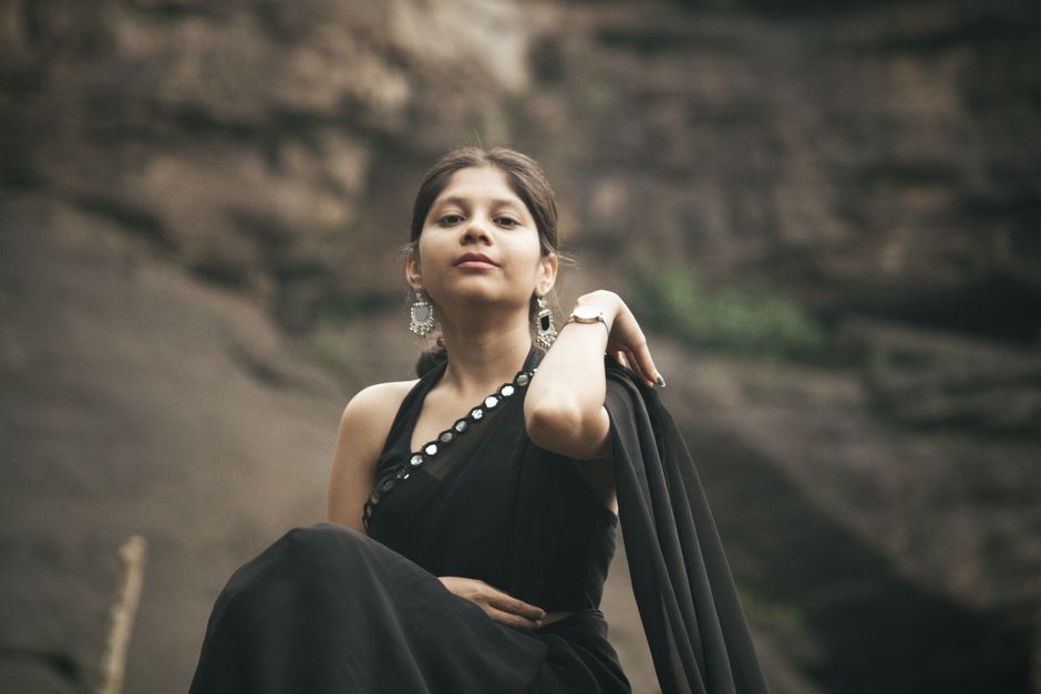 Confident woman in a black saree posing against a rocky background in Pariyaram, India.