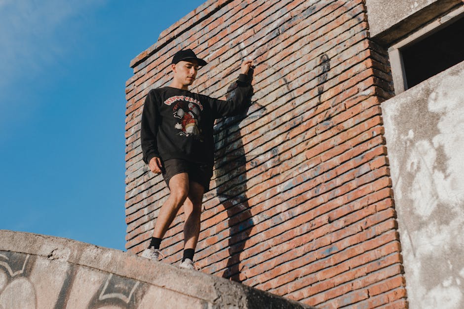 Man posing by a brick wall in urban scenery, showcasing street fashion.