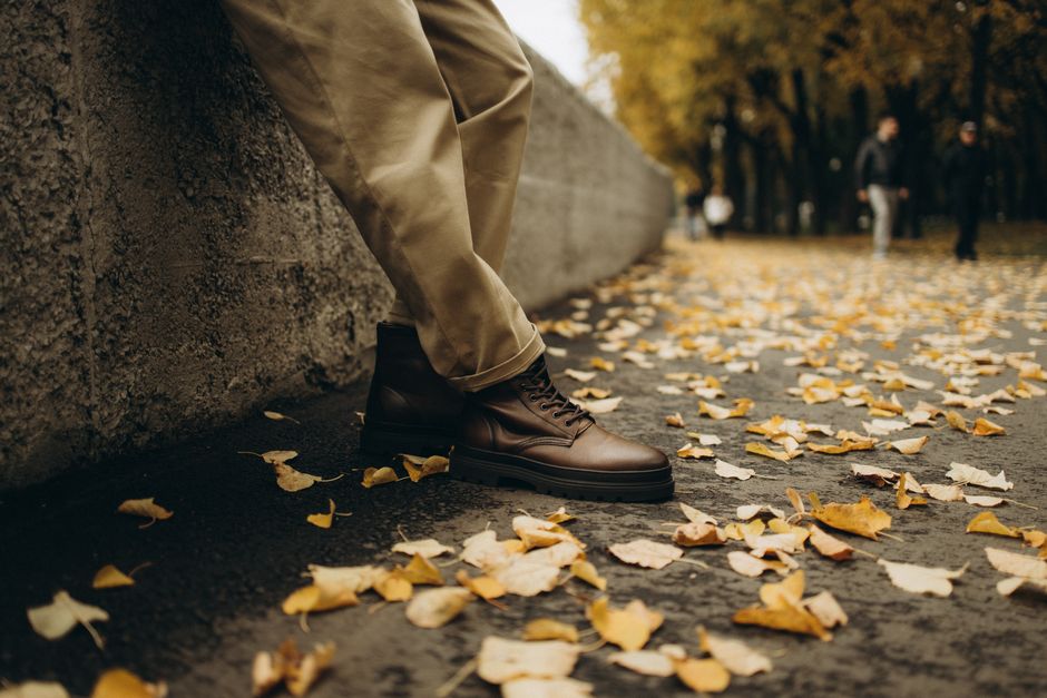 Close-up of brown leather boots on a leaf-covered path in autumn park setting.