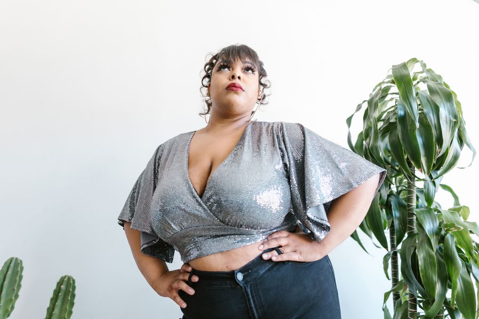 Portrait of a confident plus size woman in a sparkling silver top with hands on hips, exuding elegance.