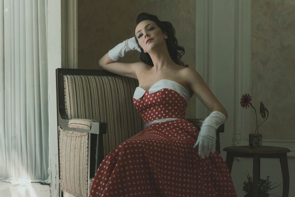 A woman in a vintage polka dot dress poses elegantly indoors with a classic vibe.