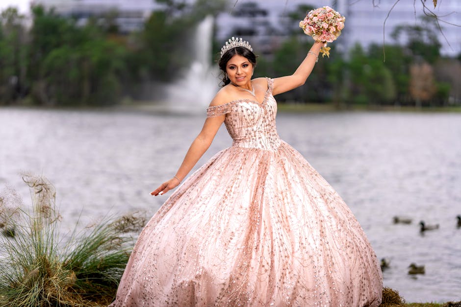 A young woman celebrates her quinceañera in a stunning gown by a scenic lake, holding a bouquet.